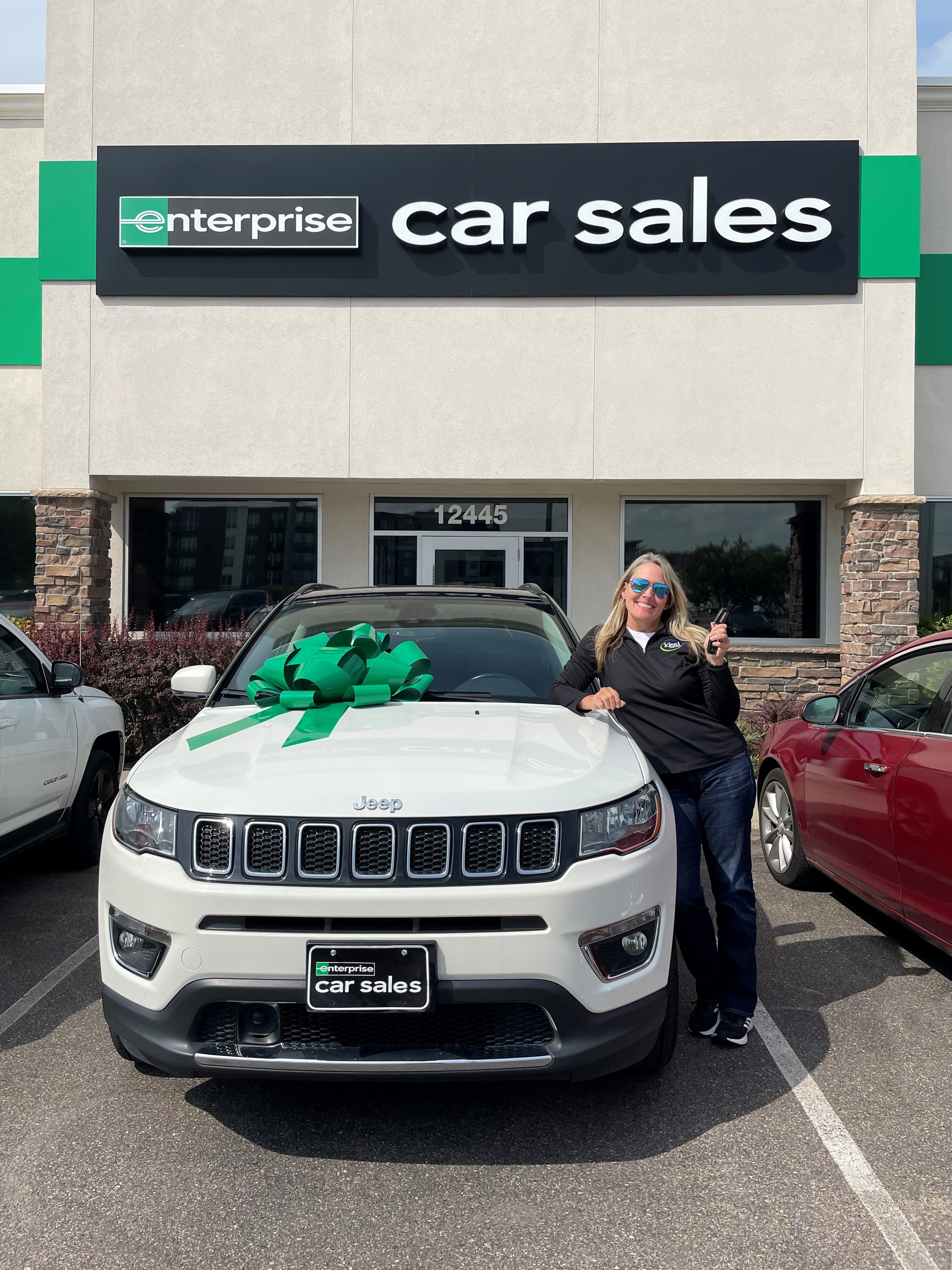 woman standing next to vehicle on car sales lot with enterprise license plate